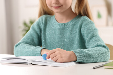 Girl using eraser at white desk indoors, closeup