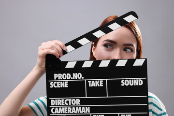 Emotional actress with clapperboard on grey background. Film industry