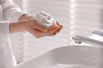 Woman washing hands with cleansing foam near sink in bathroom, closeup. Space for text