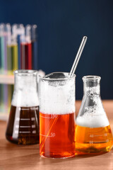 Laboratory glassware with colorful liquids on wooden table, closeup. Chemical reaction