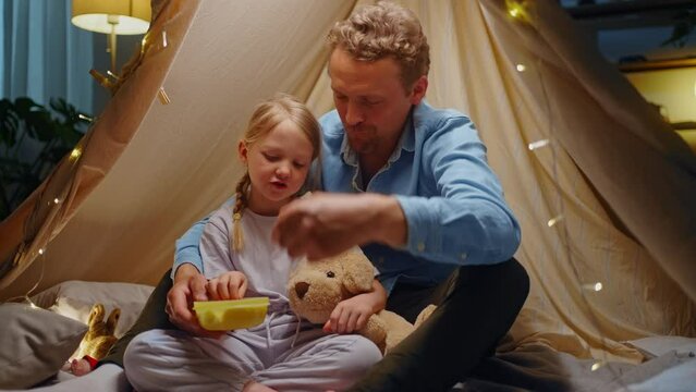 Portrait of father and daughter play camping together on floor with tent, snack with biscuits