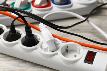 Power strip with extension cords on white wooden floor, closeup. Electrician's equipment