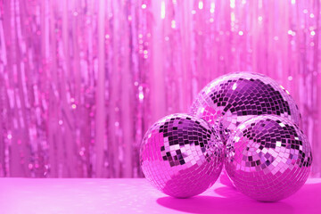 Shiny disco balls on table against blurred background, toned in pink. Space for text