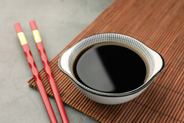 Bowl of soy sauce and chopsticks on grey table closeup