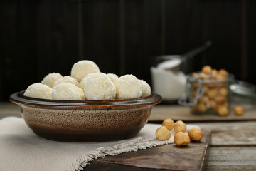 Delicious candies with coconut flakes and hazelnut on wooden table, space for text