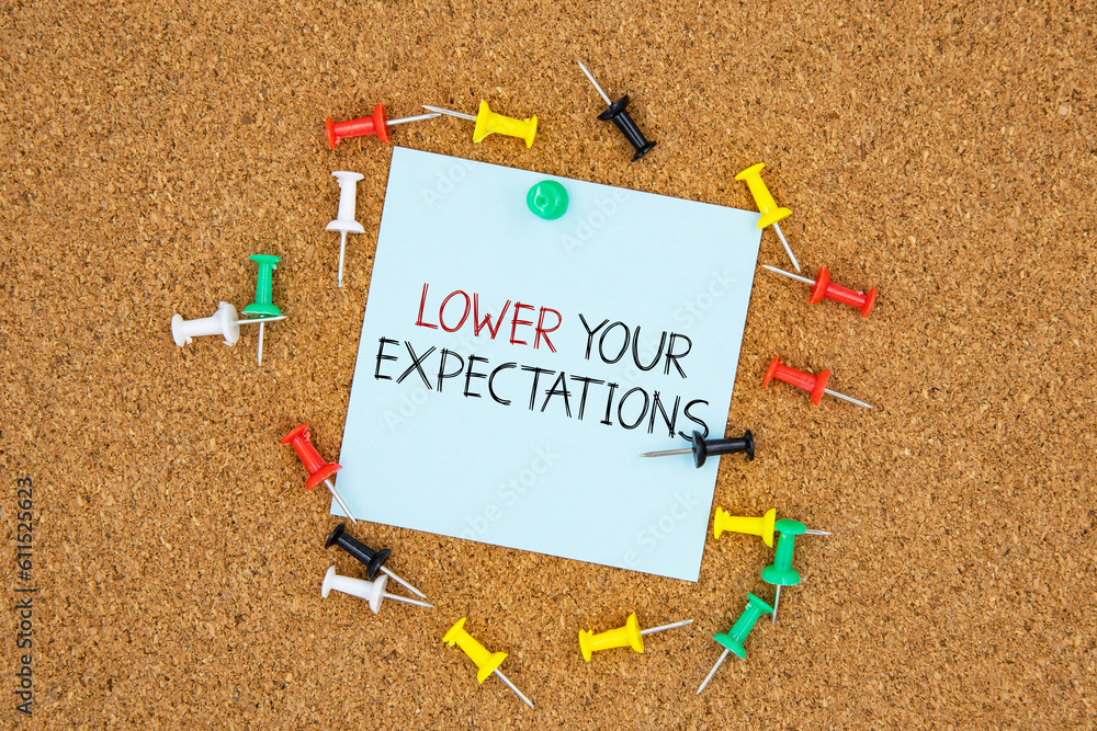 Poster lower your expectations text on light blue post-it paper pinned on bulletin cork board surrounding b