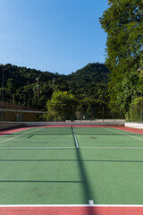 Fototapeta premium View of a green and red tennis court with nature all around. Widely used for sports and playing tennis