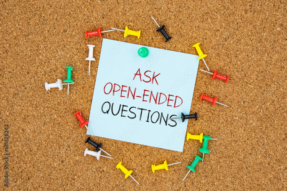 Poster ask open-ended questions text on light blue post-it paper pinned on bulletin cork board surrounding 