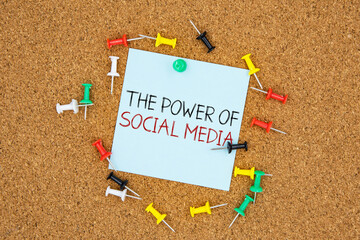 The power of social media text on light blue post-it paper pinned on bulletin cork board surrounding by multi color pins. This message can be used in business concept about the power of social media.