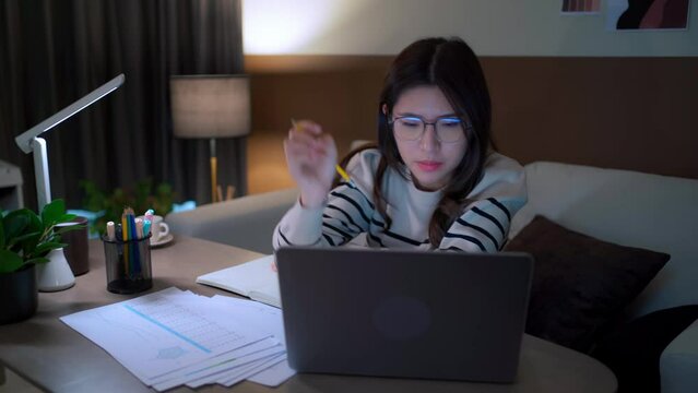 Tried Asian women working overtime in front of the computer at night make their eyes dizzy. young lady removes her glasses and shaking head with closed eyes. Overtime work concept