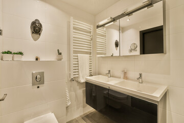 a modern bathroom with white tiles and black countertops, along with a tv mounted on the wall above the sink