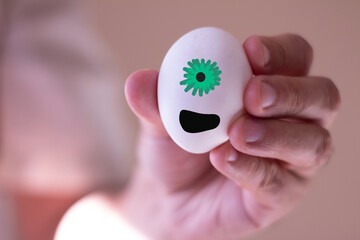 Egg with the face of an alien and a spare expression being held by a man's hand.