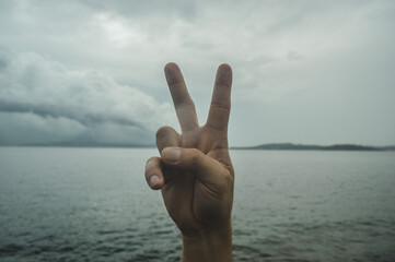 gesturing with the hand, on an exterior background of sea and sky, two or peace symbols