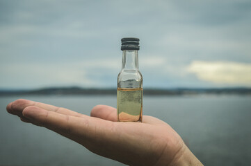 hand holding a small bottle with liquid inside, on a background of sea and sky