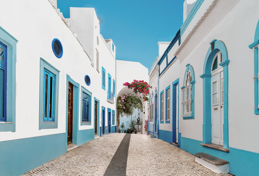 Street in fishermen village with white and blue houses and typical Portuguese pavement in Olhao, Algarve region - Popular travel destinations in Portugal