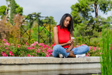 Young mother thoughtful, with a flower outdoors in a park.