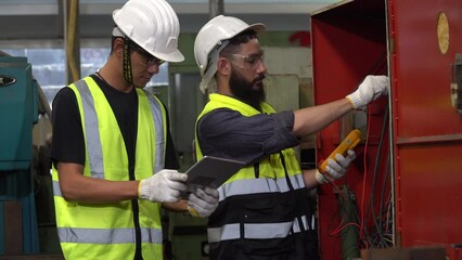 group of two diversity Electrician engineer checking electrical installations and wires on cabinet with tablet computer in factory . team arab and asian repairman maintenance in manufacturing industry