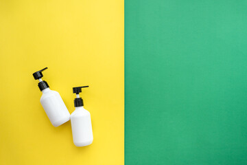 White Dispenser on green and yellow Background, top view, copy space. Blank plastic pump bottle for...
