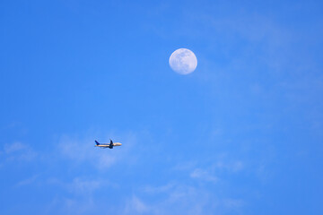 東の空に昇った小望月とその下を飛ぶ旅客機