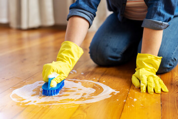 Woman in rubber gloves is using floor brush to cleaning floor