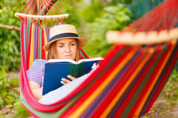 Young woman reading book while lying in comfortable hammock at green garden