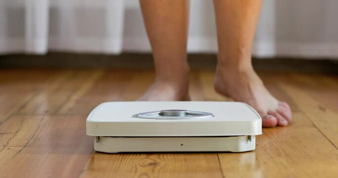 A woman stands on white scale on the floor and measures her weight