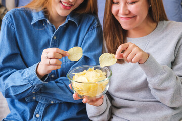 Closeup image of a young couple women sharing and eating potato chips together