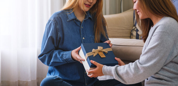 Closeup image of a young couple women giving and receiving a gift box to each other