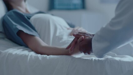 Young female patient lying on medical couch in a hospital ward, holding hands with doctor and looking at her, getting support during treatment. Tilt-down shot