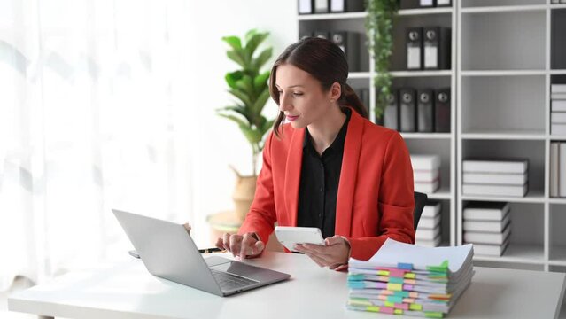 Confident business expert attractive smiling young woman typing laptop ang holding digital tablet on desk in office..