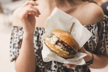 young woman holds a fast food burger in craft packaging in her hands. Street food. Woman has quick...