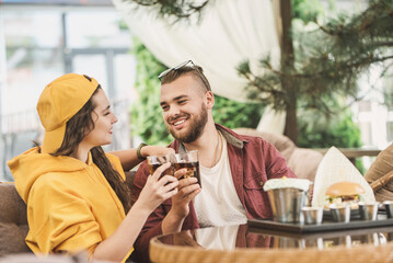 Young couple in love having fun spending leisure time together at restaurant, eating burgers and drinking cola