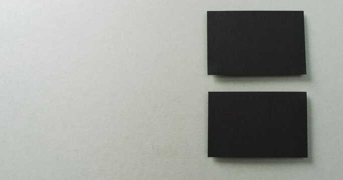 Overhead view of two black business cards arranged on grey background, copy space, slow motion