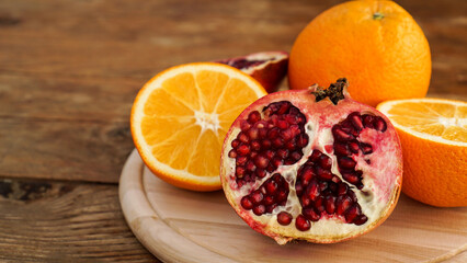 Fototapeta na wymiar Pomegranate and oranges on a wooden background. Cut fruit