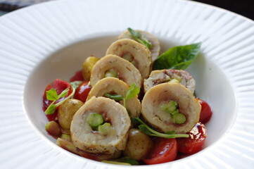 Sliced asparagus stuffed chicken breast roll with cherry tomatoes and grilled potato in white rim...
