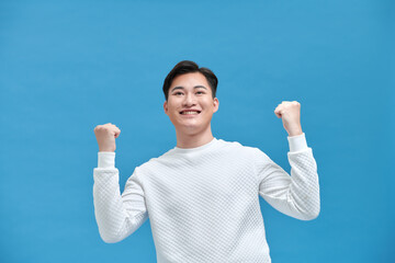Happy guy rejoicing and clenching fists like winner or lucky person, isolated over blue background