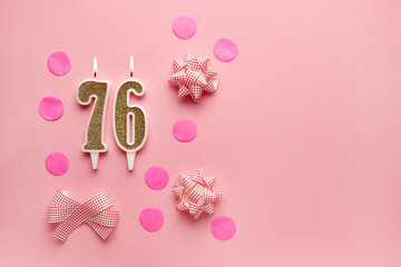 Number 76 on pastel pink background with festive decor. Happy birthday candles. The concept of...