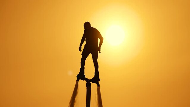 Epic scene at sunset. Athlete flyboarder on the background of the sunset sky and the sun. The silhouette of a man flies in the sky at sunset.