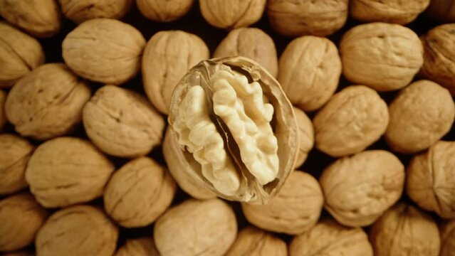 A top-down view of a partially peeled walnut slowly rotating and falling down among a pile of other nuts. Macro slide, in slow motion.
