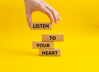 Listen to your heart symbol. Concept word Listen to your heart on wooden blocks. Beautiful yellow background. Businessman hand. Business and Listen to your heart concept. Copy space