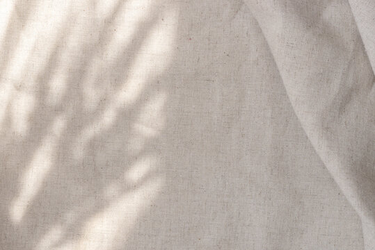 Aesthetic boho wedding textile background, draped neutral beige linen fabric texture with absrtact floral sunlight shadows