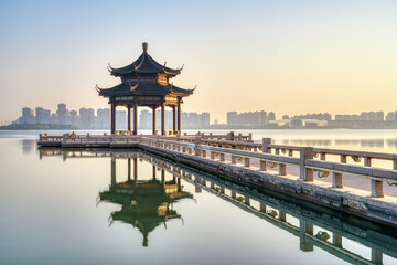 A pavilion and its reflection in the lake. Modern skyscrapers in distance. Photo is taken in Suzhou, Jiangsu province, China.