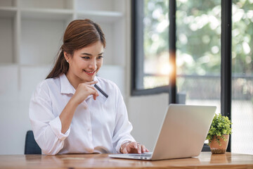 Beautiful young Asian woman holding smartphone and using credit card for online shopping.