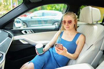 A young girl drinks coffee in the car and use smartphone