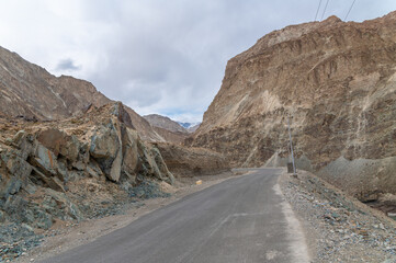 A concrete road towards beautiful rocky mountains and blue sky with peaks of Himalaya, Leh, Ladakh, India