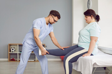 Physiotherapist examines an overweight female patient. Side view of a man doctor in a uniform doing...