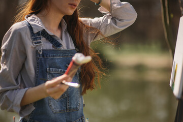 A woman in overalls is holding a paintbrush and color paint