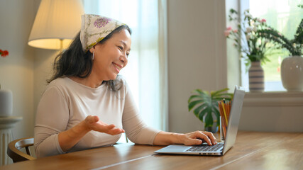 Positive stylish middle age woman having video call with family or friends on laptop. People, technology and communication concept