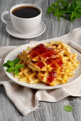 Belgian waffles with strawberry jam and coffee on a gray background