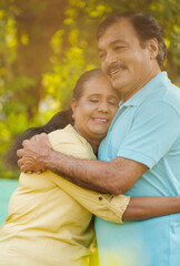 Obraz premium vertical shot of Happy indian elderly senior woman embracing or hugging husband by holding closely with added sun flare effect - concept of companion, secure and comfortable